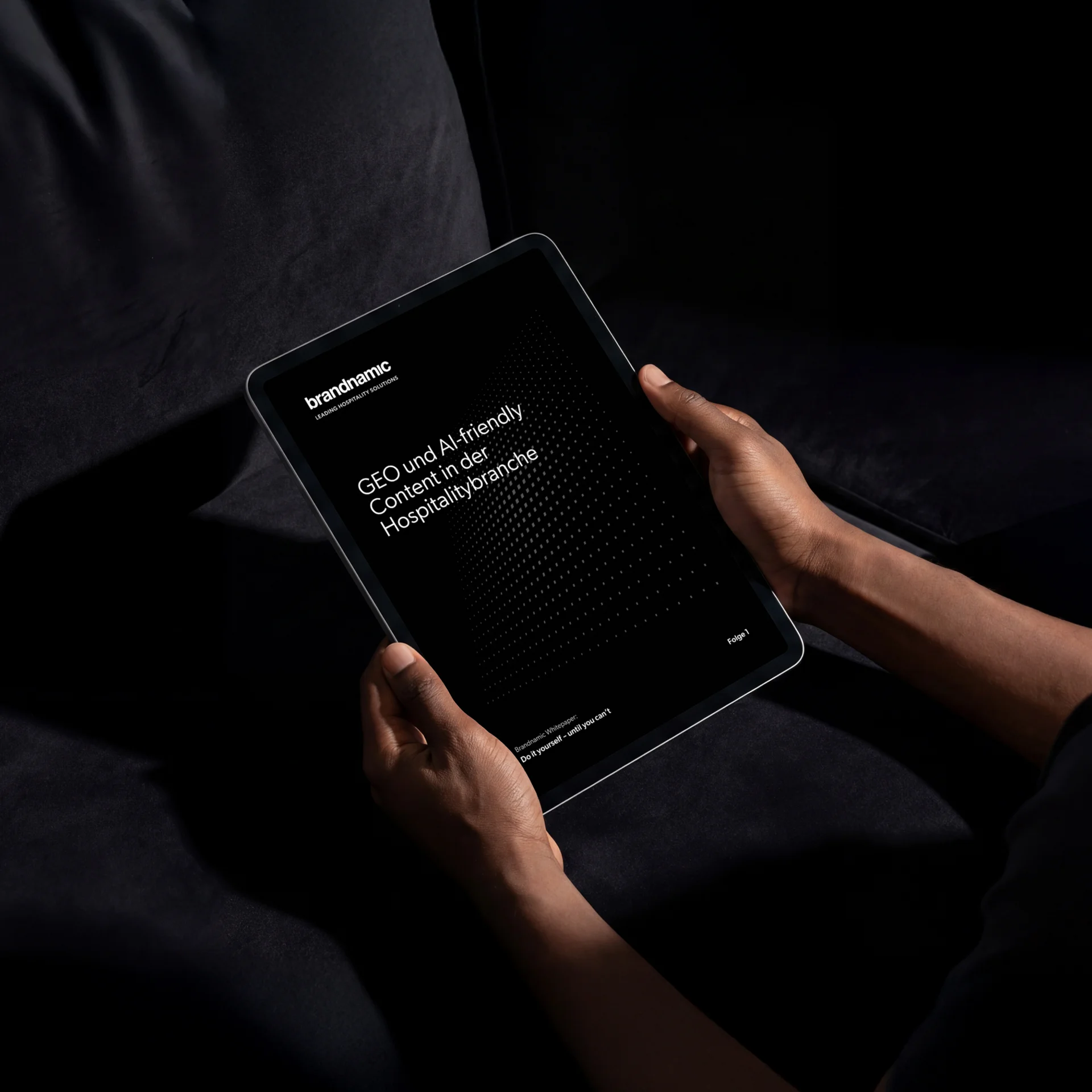GEO und AI-friendly Content in der Hospitalitybranche Person hält Tablet mit schwarzem Bildschirm und weißem Text vor dunklem Hintergrund