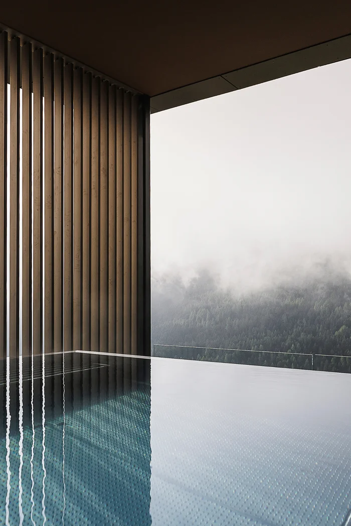 Infinity-Pool mit Holzwand und Nebel über bewaldeten Bergen