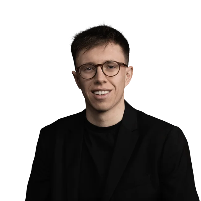 Junger Mann mit brauner Brille in schwarzem Anzug vor weißem Hintergrund