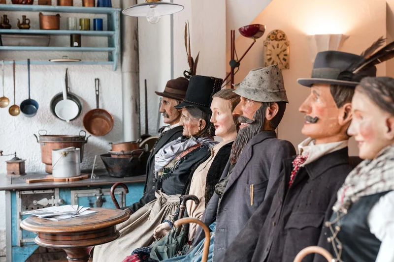 Row of life-sized wooden dolls dressed in traditional clothes in an old room