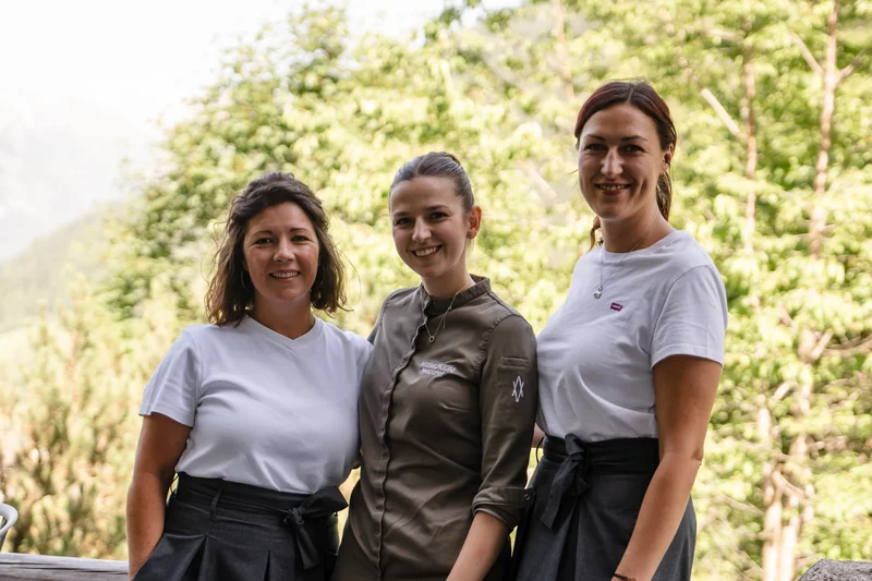 Drei lächelnde Frauen posieren draußen vor grünen Bäumen