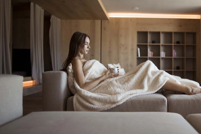 Frau entspannt auf Sofa mit Decke und Tasse in modernem Wohnzimmer