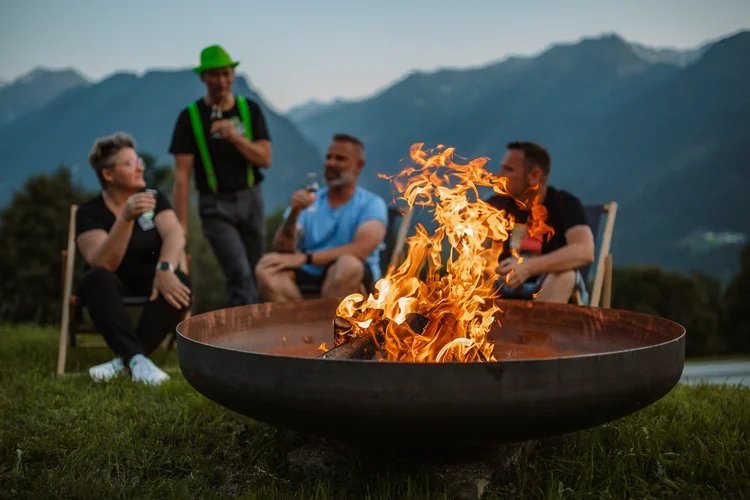 Storytelling im Hotelmarketing Vier Männer sitzen und stehen am Feuerkorb vor einer Bergkulisse