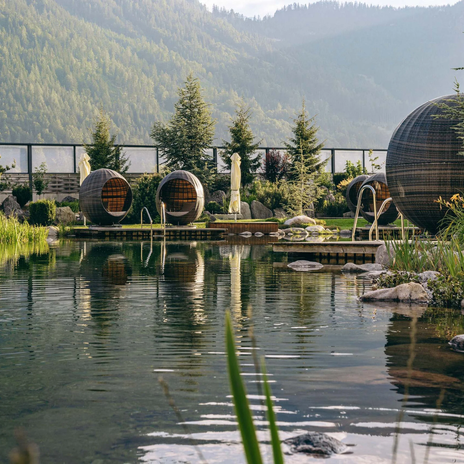 Familienhotel Buchau am Achensee Natürlicher Schwimmteich mit modernen Sitzkapseln und Bergkulisse