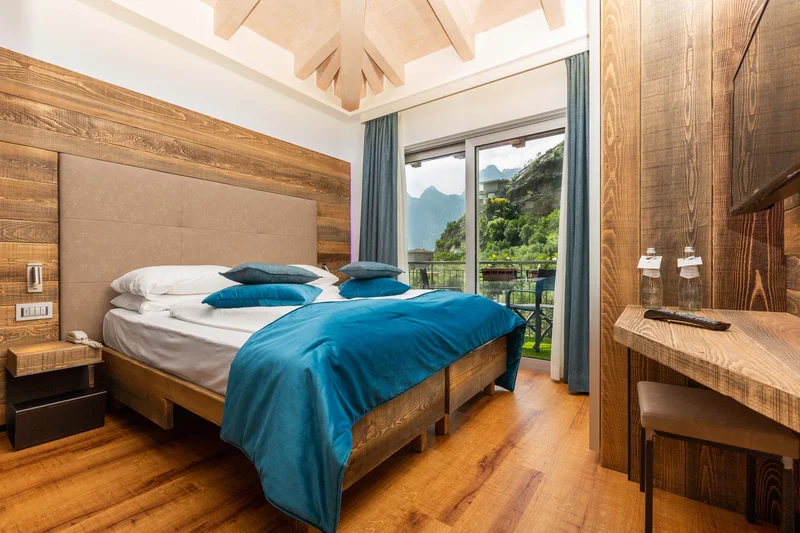 AktivHotel SantaLucia: Vom Tool-Chaos zur digitalen Einheit am Gardasee Gemütliches Schlafzimmer mit Holzdekor und Bergblick durch große Fenster
