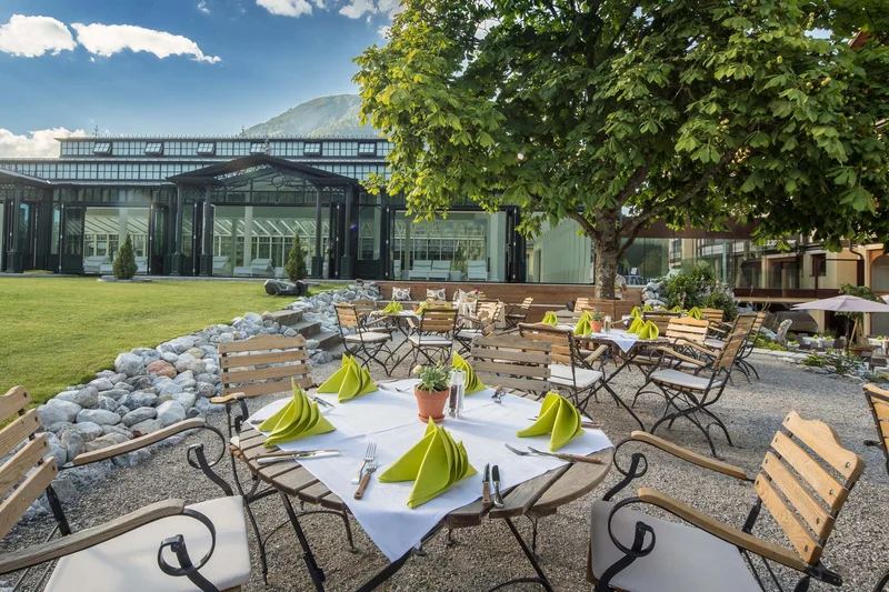Gartenrestaurant mit Holztischen und grünen Servietten vor einem verglasten Gebäude