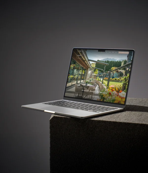 Two worlds, one signature Laptop displaying a website with a sunny garden and terrace on a dark pedestal