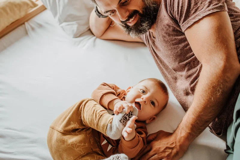 Das Mühlwald: perfectly visible Father smiling and playing with baby on bed