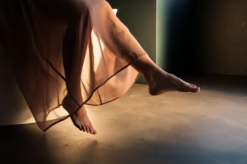Beine einer Frau im transparenten Kleid, die in einem dunklen Raum schweben