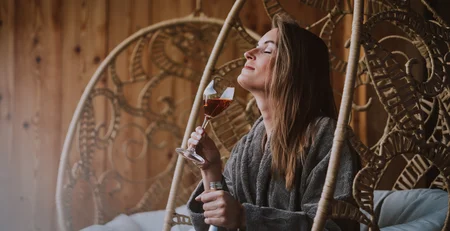 Woman relaxing in hanging chair with wine glass and bottle in wooden interior