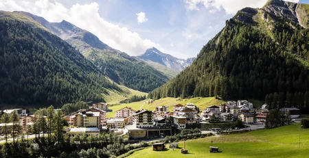 Die besten Referenzen für unser Hotelmarketing Idyllisches Bergdorf umgeben von grünen Wäldern und Bergen bei klarem Himmel