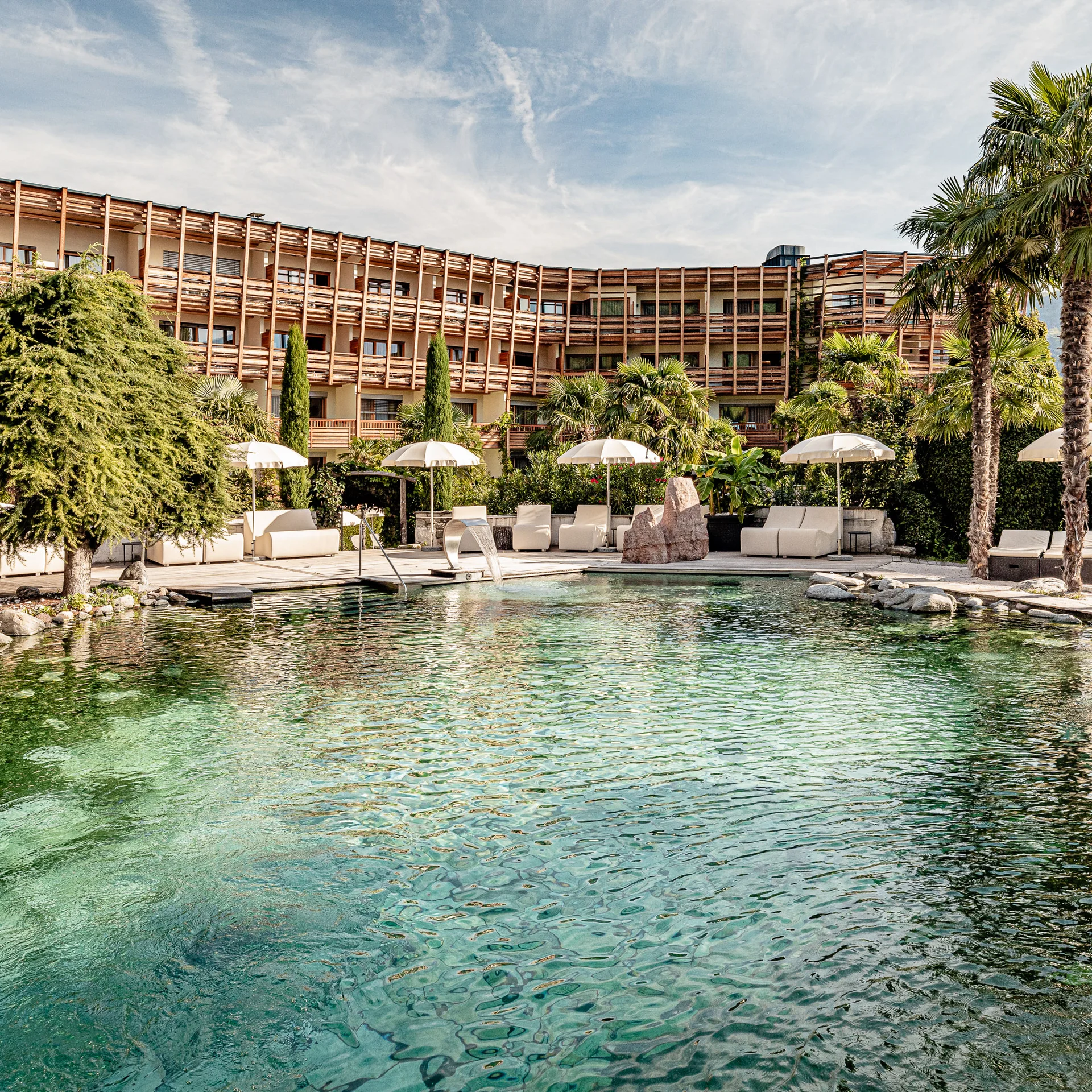 Immerse yourself in Italian dolce vita Hotel pool with natural water, palm trees, and lounge chairs under a blue sky