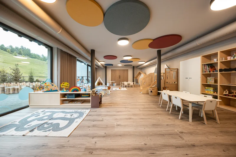 Bright children's playroom with wooden toys, tables, chairs, and large windows