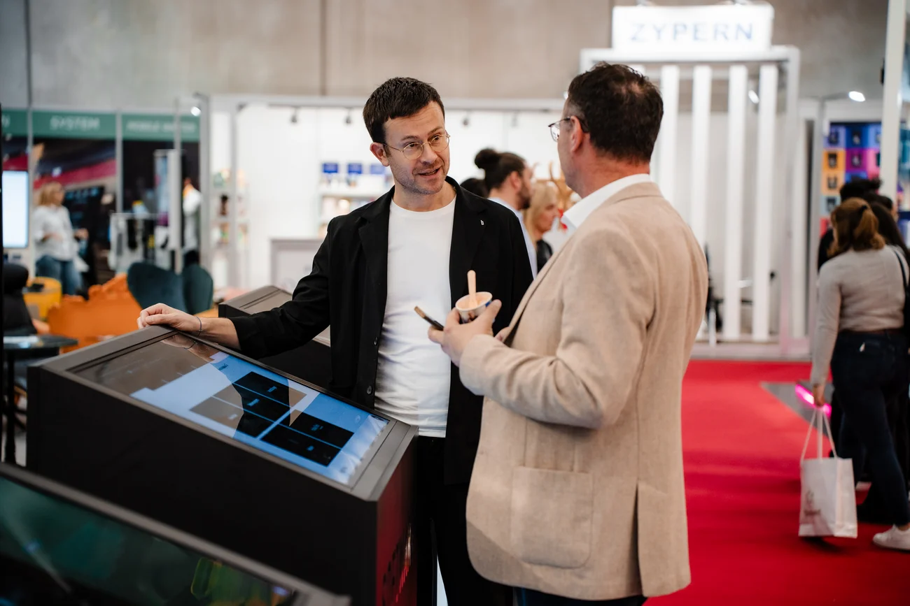 Zwei Männer unterhalten sich an einem Touchscreen-Display auf einer Messe