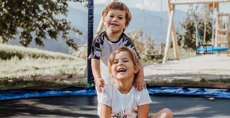Die besten Referenzen für unser Hotelmarketing Zwei lachende Kinder spielen auf einem Trampolin im Freien bei Sonnenschein