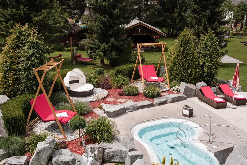 Garten mit Pool, roten Liegen und mehreren Bäumen in einer Berglandschaft