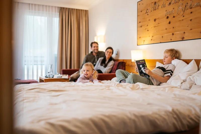 Familienhotel Buchau am Achensee Familie entspannt im Hotelzimmer mit Kind liest Buch auf dem Bett
