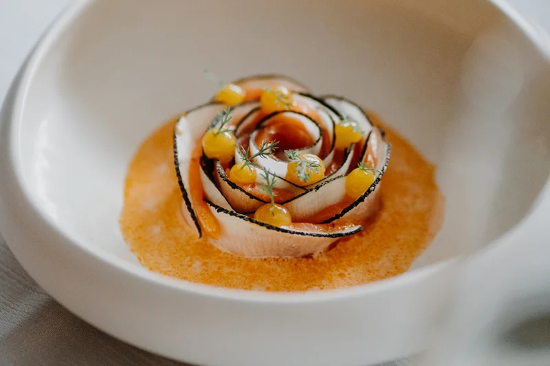Two worlds, one signature Creative dish with curled slices, orange sauce, yellow dots and fresh herbs