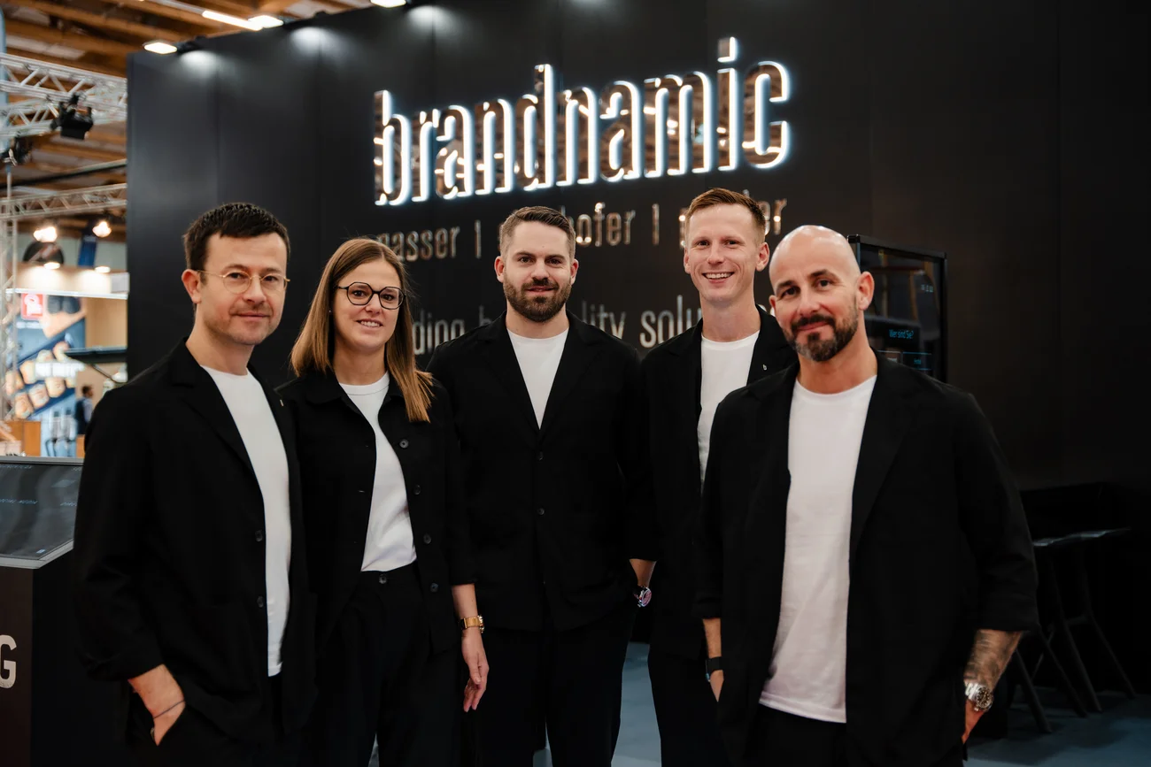 Fünf Personen vor einem Brandnamic-Messestand stehen und lächeln